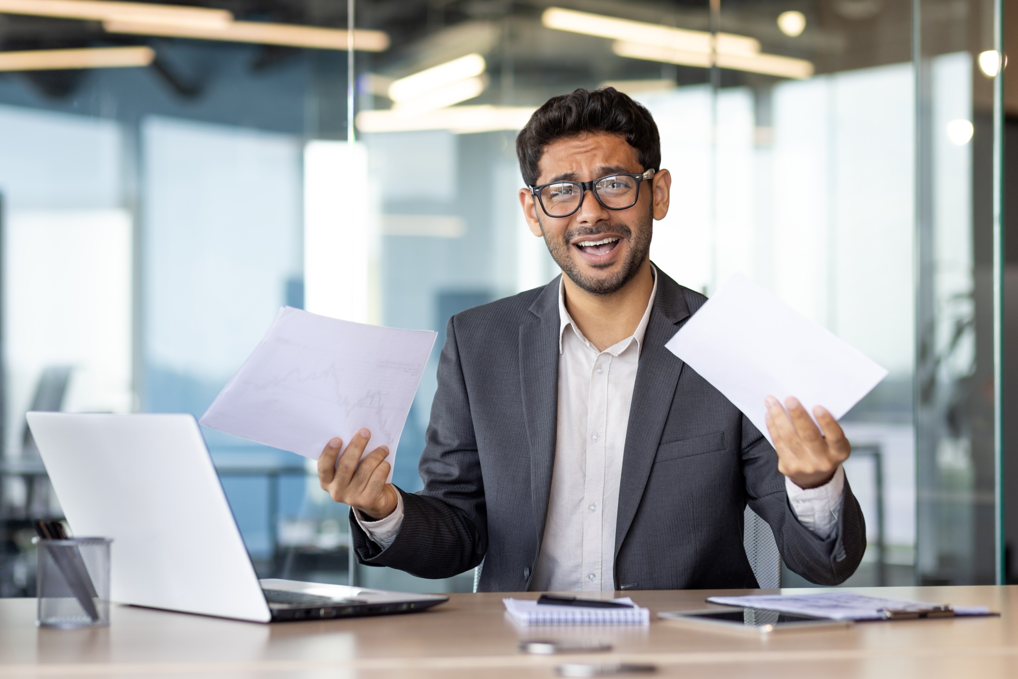 Upset and disappointed businessman financier investor looking at camera, man holding papers reports